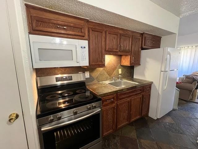 kitchen featuring white appliances, stone tile floors, tasteful backsplash, a textured ceiling, and a sink