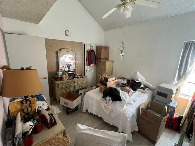 bedroom featuring a ceiling fan, vaulted ceiling, light wood-style flooring, and a textured ceiling