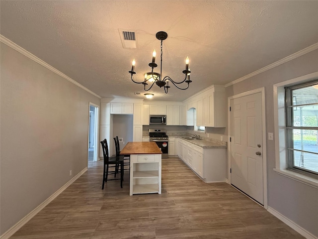 kitchen featuring stainless steel appliances, wood finished floors, white cabinets, an inviting chandelier, and crown molding