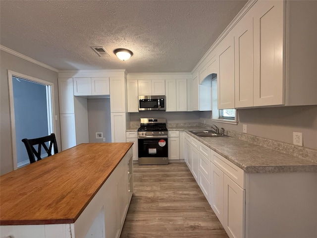 kitchen featuring stainless steel appliances, butcher block counters, white cabinets, a sink, and wood finished floors