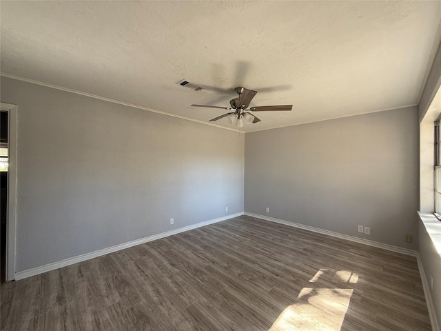 empty room with ceiling fan, visible vents, baseboards, ornamental molding, and dark wood finished floors