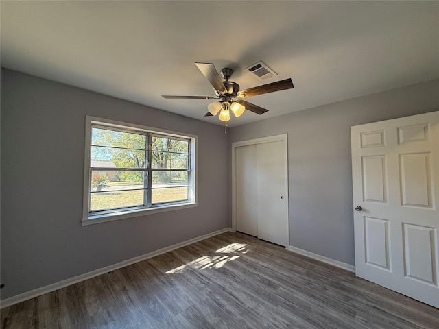 unfurnished bedroom featuring baseboards, visible vents, ceiling fan, wood finished floors, and a closet