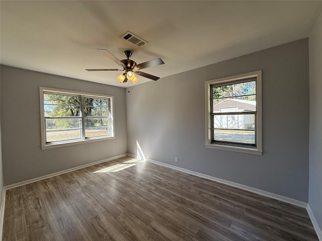 unfurnished room featuring dark wood-type flooring, plenty of natural light, visible vents, and baseboards