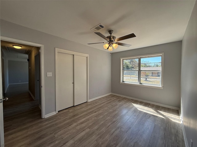 unfurnished bedroom with a closet, visible vents, attic access, dark wood-type flooring, and baseboards