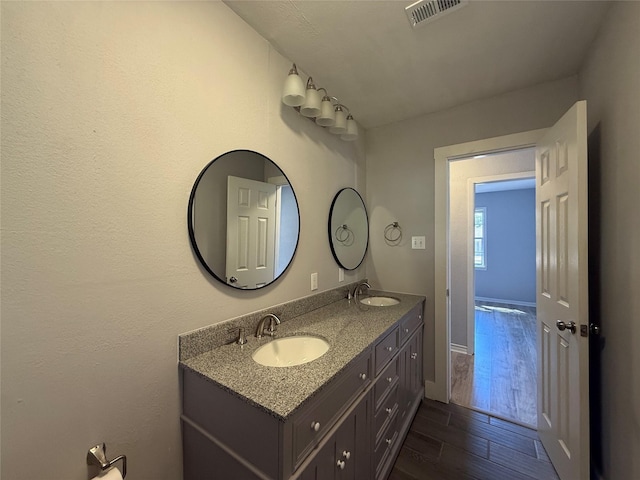 bathroom with double vanity, visible vents, a sink, and wood finished floors