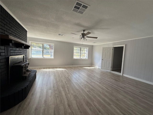 living room featuring a textured ceiling, wood finished floors, visible vents, a wood stove, and crown molding