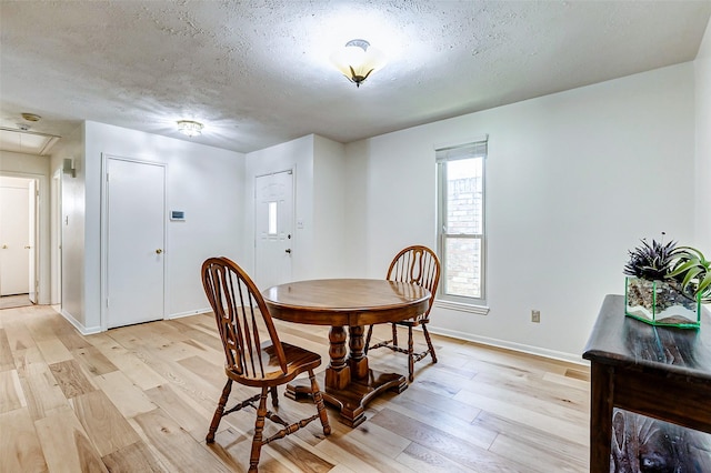 dining room featuring light wood finished floors, attic access, baseboards, and a textured ceiling