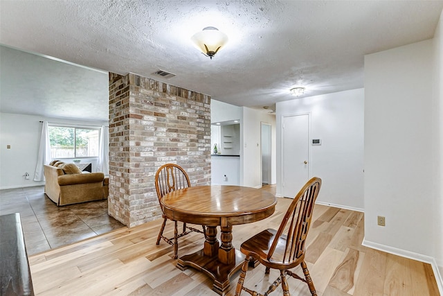 dining room featuring a textured ceiling, light wood-type flooring, visible vents, and baseboards