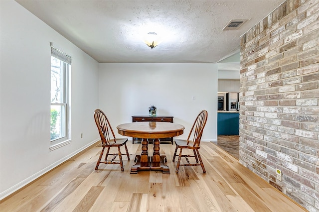 dining space with baseboards, visible vents, a textured ceiling, and light wood finished floors