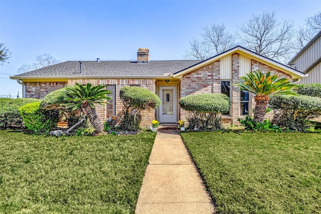 view of front of house featuring brick siding, a chimney, a front yard, and a shingled roof