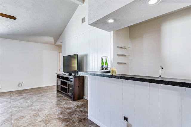 kitchen with lofted ceiling, a textured ceiling, dark countertops, and visible vents