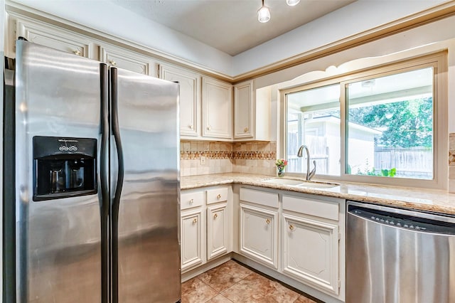 kitchen with light tile patterned floors, stainless steel appliances, tasteful backsplash, a sink, and light stone countertops