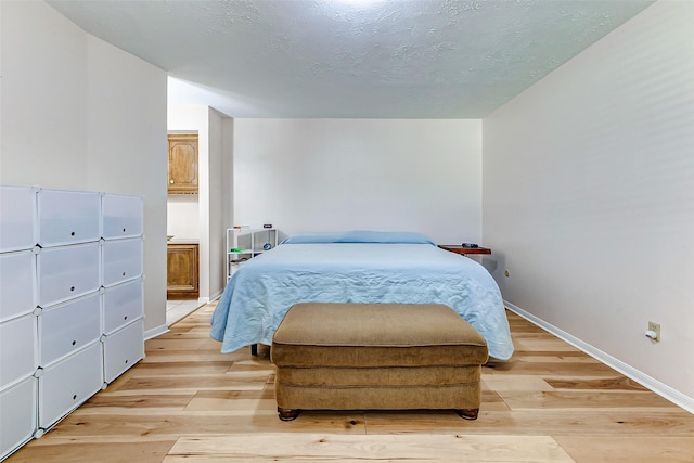 bedroom featuring light wood-type flooring, baseboards, and a textured ceiling