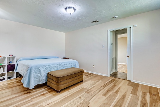 bedroom with baseboards, visible vents, a textured ceiling, and light wood finished floors