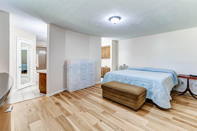 bedroom with light wood-style flooring, baseboards, a textured ceiling, and ensuite bathroom