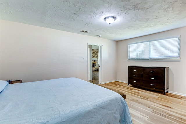 bedroom featuring a textured ceiling, wood finished floors, visible vents, and baseboards