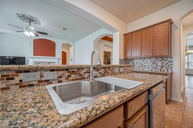 kitchen featuring light tile patterned floors, tasteful backsplash, brown cabinetry, a sink, and dishwasher