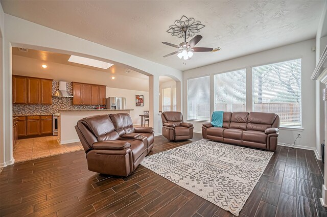 living room featuring arched walkways, ceiling fan, wood finish floors, and baseboards