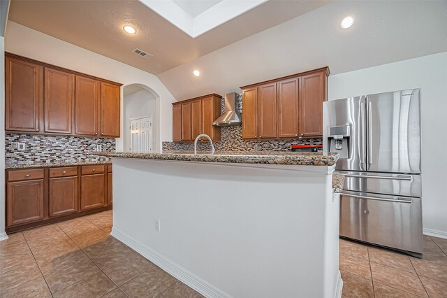 kitchen featuring light stone counters, stainless steel refrigerator with ice dispenser, light tile patterned floors, visible vents, and wall chimney exhaust hood