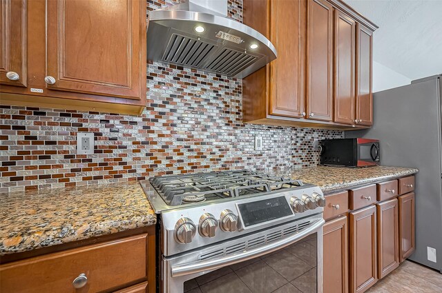 kitchen featuring stainless steel gas stove, tasteful backsplash, light stone counters, wall chimney range hood, and black microwave