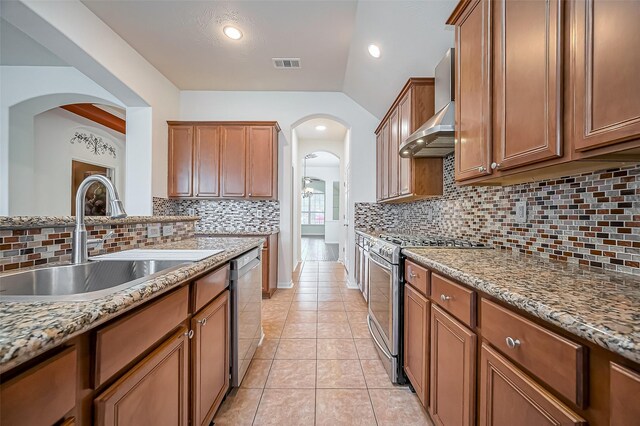 kitchen with light tile patterned flooring, a sink, vaulted ceiling, wall chimney range hood, and appliances with stainless steel finishes