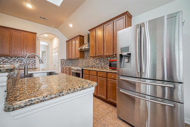 kitchen with lofted ceiling, a sink, visible vents, appliances with stainless steel finishes, and wall chimney range hood