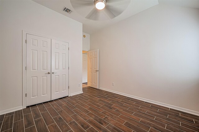 unfurnished bedroom with baseboards, visible vents, lofted ceiling, dark wood-style floors, and a closet