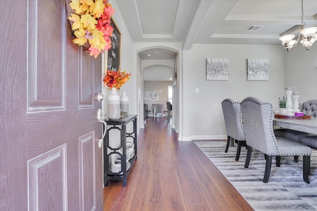 dining space featuring arched walkways, a chandelier, wood finished floors, visible vents, and baseboards