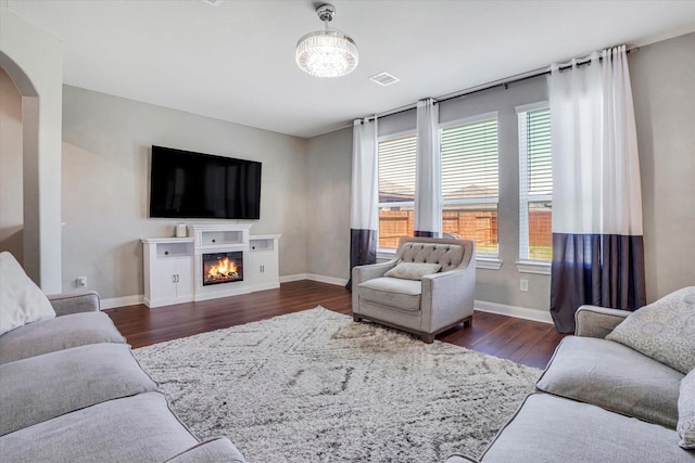 living room featuring baseboards, arched walkways, wood finished floors, and a glass covered fireplace