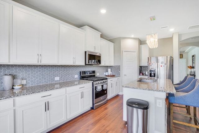 kitchen with arched walkways, a breakfast bar area, appliances with stainless steel finishes, a sink, and light wood-type flooring