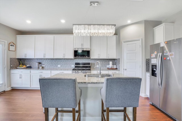 kitchen with stainless steel appliances, a sink, decorative backsplash, and wood finished floors