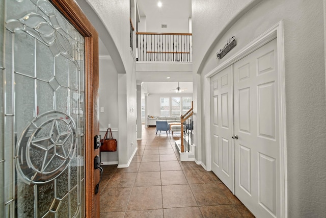 tiled foyer with arched walkways, a towering ceiling, stairway, ceiling fan, and baseboards