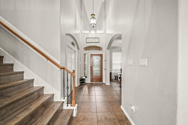 tiled foyer with stairway, baseboards, arched walkways, and a textured wall