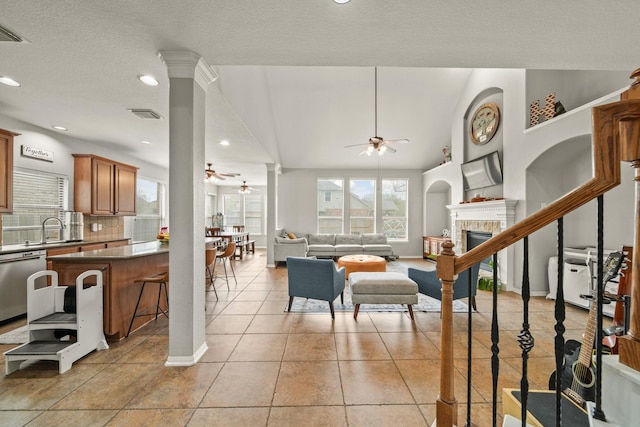 living area featuring light tile patterned floors, decorative columns, a tile fireplace, and a ceiling fan