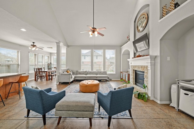 living room with ornate columns, ceiling fan, a wealth of natural light, and a glass covered fireplace