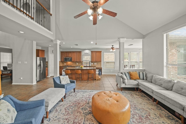 living room with ornate columns, a ceiling fan, light tile patterned flooring, high vaulted ceiling, and baseboards