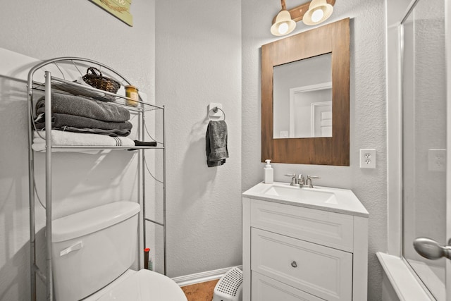 bathroom featuring baseboards, a textured wall, toilet, a shower with door, and vanity