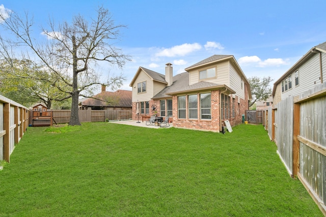 back of house featuring brick siding, a patio, a chimney, a lawn, and a fenced backyard