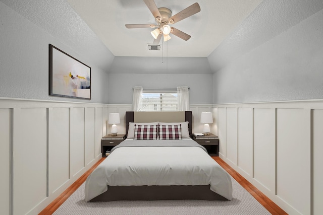 bedroom featuring lofted ceiling, a wainscoted wall, visible vents, and wood finished floors