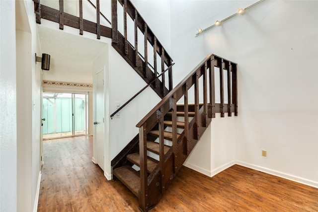 staircase featuring a towering ceiling, baseboards, and wood finished floors