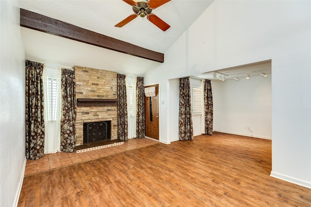 unfurnished living room with vaulted ceiling with beams, a fireplace, a textured ceiling, wood finished floors, and baseboards