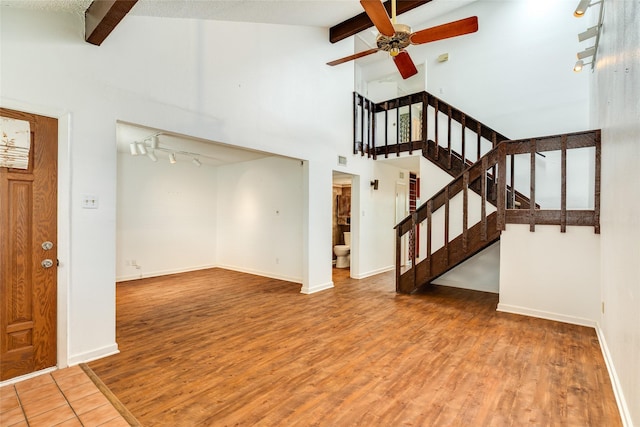 unfurnished living room with stairs, beamed ceiling, wood finished floors, and baseboards