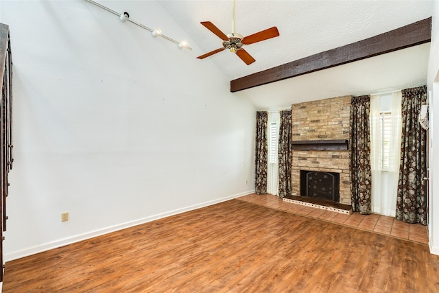 unfurnished living room with vaulted ceiling with beams, a ceiling fan, a brick fireplace, a textured ceiling, and wood finished floors