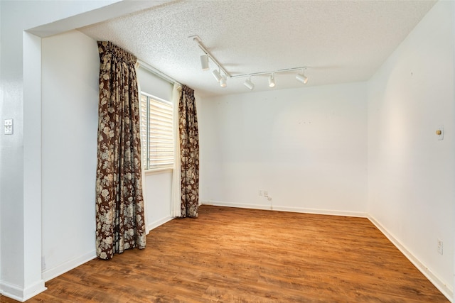 spare room with track lighting, a textured ceiling, baseboards, and wood finished floors