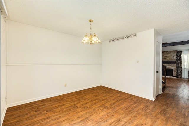 spare room with a fireplace, an inviting chandelier, a textured ceiling, wood finished floors, and baseboards