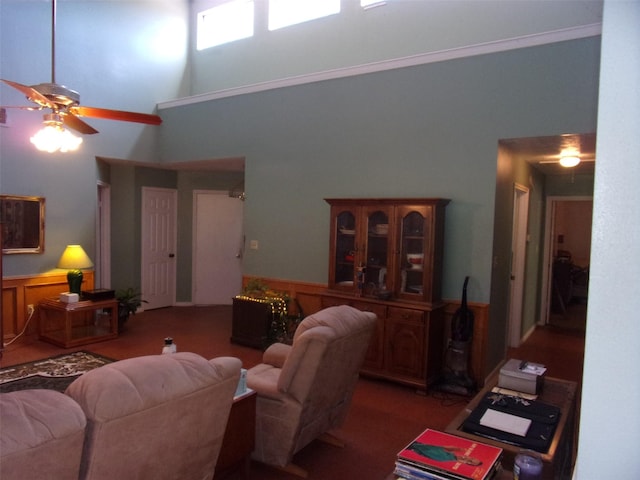 living area with a ceiling fan, a wainscoted wall, and a towering ceiling