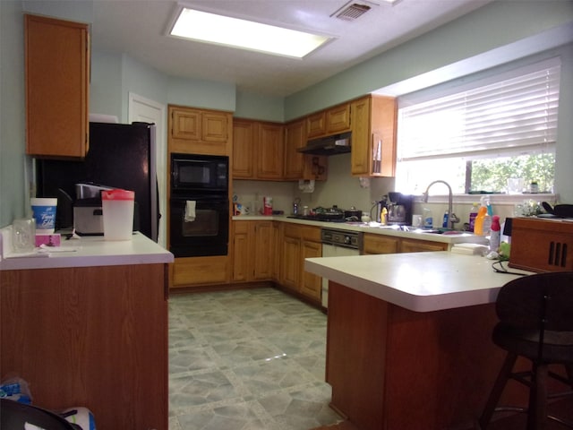 kitchen with under cabinet range hood, a peninsula, visible vents, light countertops, and black appliances