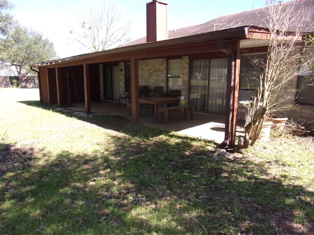 back of house with a chimney, a patio area, and a lawn