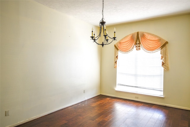 empty room featuring dark wood-style floors, a textured ceiling, and an inviting chandelier