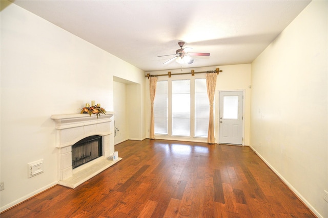 unfurnished living room with dark wood-type flooring, a fireplace with raised hearth, baseboards, and a ceiling fan